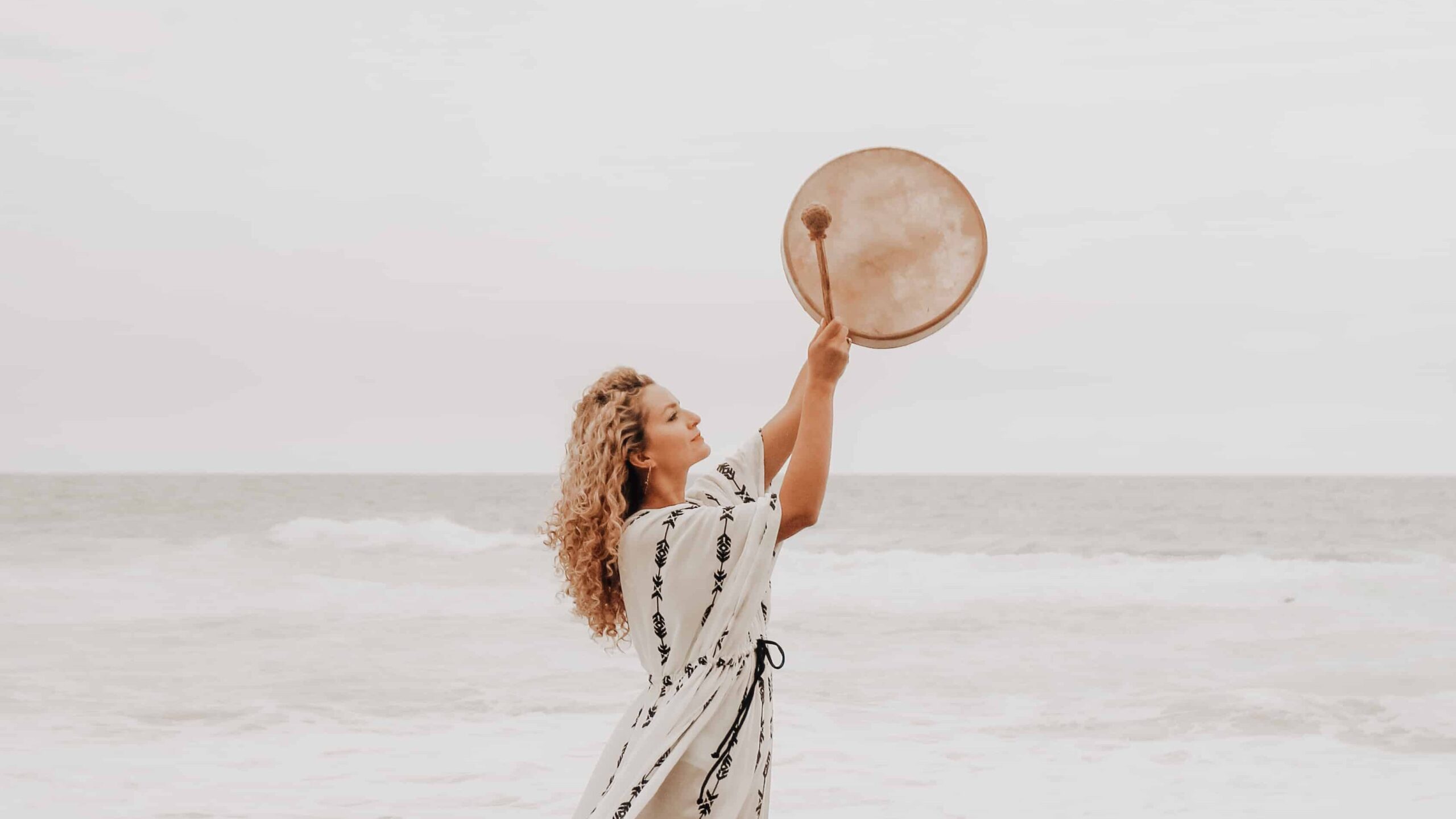 A spiritual counselor beating a shamanic drum at the ocean for soul healing